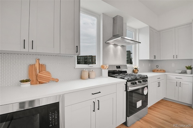 kitchen with built in microwave, tasteful backsplash, stainless steel range with gas stovetop, and wall chimney exhaust hood