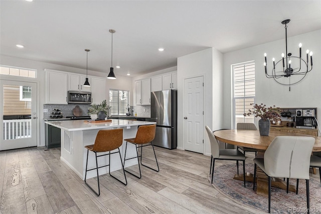 kitchen featuring a kitchen island, light wood-style floors, light countertops, appliances with stainless steel finishes, and backsplash