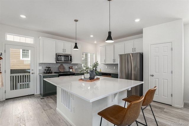 kitchen with stainless steel appliances, a center island, white cabinets, and light wood-style floors