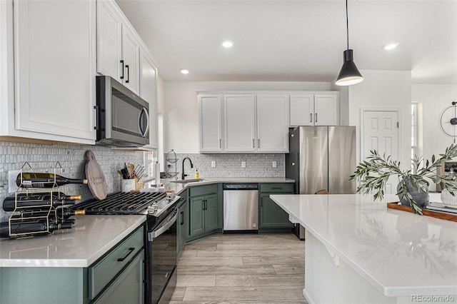 kitchen featuring light wood finished floors, decorative backsplash, stainless steel appliances, green cabinets, and a sink