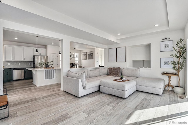 living room featuring a chandelier, recessed lighting, a raised ceiling, and light wood-style floors