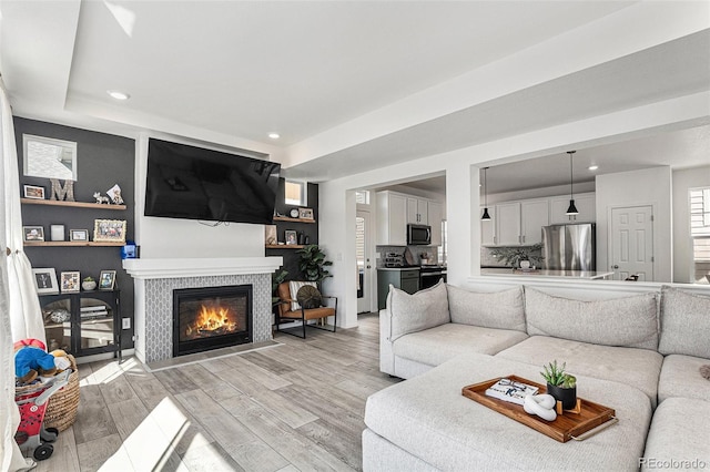 living room featuring light wood finished floors, recessed lighting, baseboards, and a glass covered fireplace