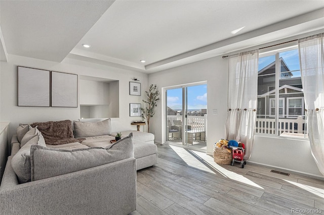 living area with recessed lighting, visible vents, a tray ceiling, and wood finished floors