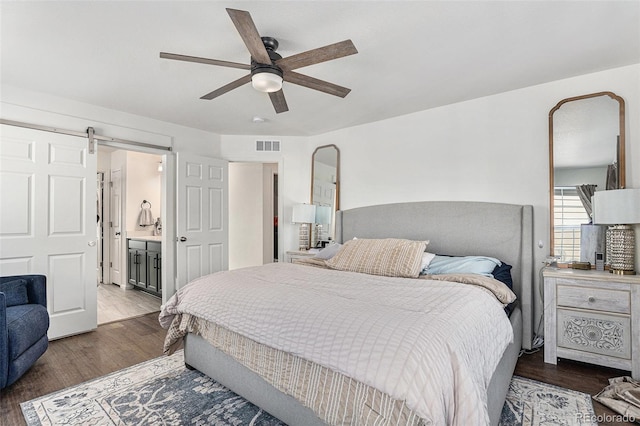 bedroom featuring a barn door, visible vents, ensuite bath, ceiling fan, and wood finished floors