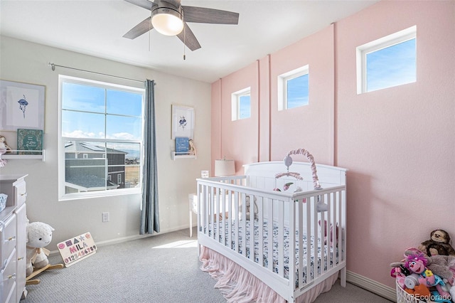 carpeted bedroom featuring a nursery area, ceiling fan, and baseboards