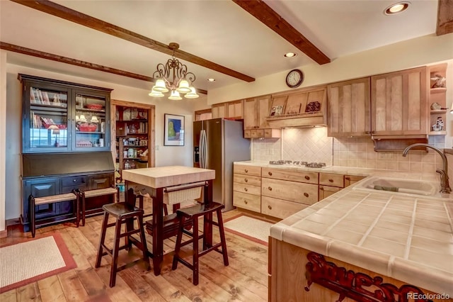 kitchen with stainless steel refrigerator with ice dispenser, beamed ceiling, hanging light fixtures, tile countertops, and sink