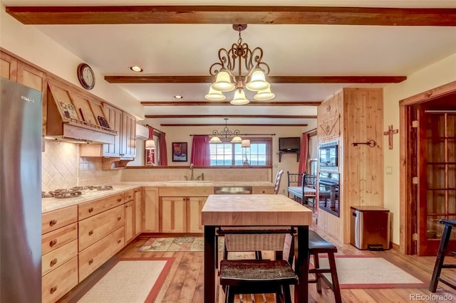 kitchen with premium range hood, stainless steel appliances, pendant lighting, sink, and light hardwood / wood-style flooring