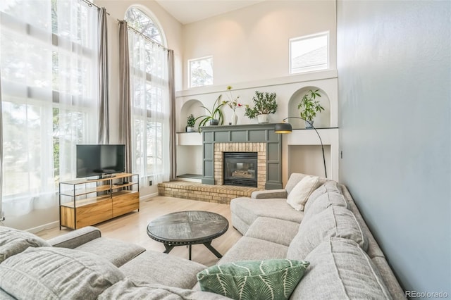 living area with a towering ceiling, a brick fireplace, and wood finished floors