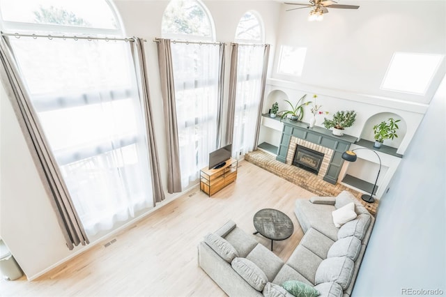 living area featuring a ceiling fan, a brick fireplace, and wood finished floors