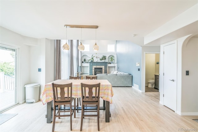 dining area featuring light wood-type flooring, baseboards, a stone fireplace, and arched walkways