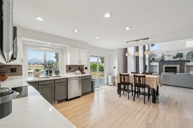 kitchen featuring stainless steel dishwasher, a sink, recessed lighting, decorative backsplash, and a fireplace