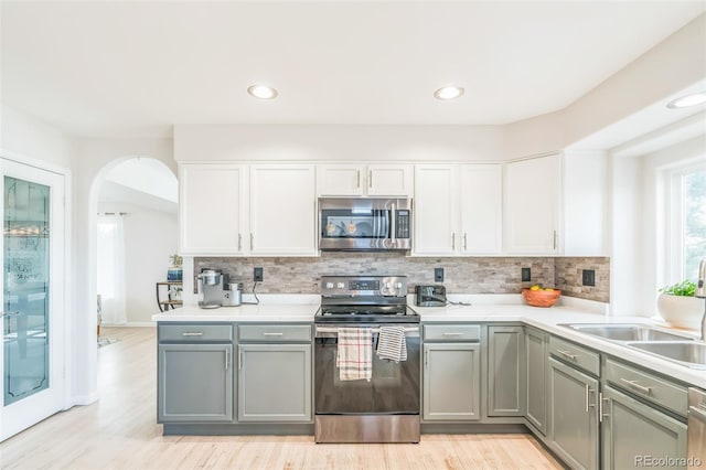 kitchen featuring stainless steel appliances, arched walkways, a sink, and gray cabinets