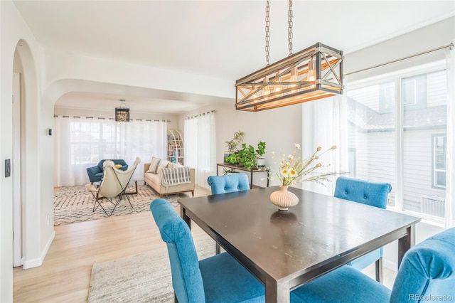 dining area with arched walkways, a chandelier, and wood finished floors