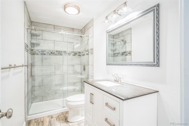full bathroom featuring toilet, wood finished floors, vanity, and a stall shower