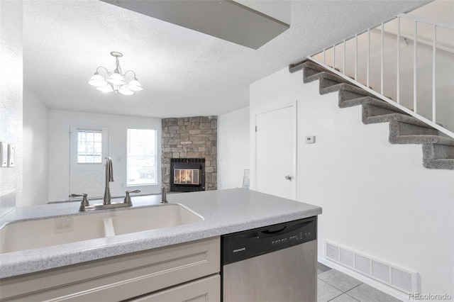 kitchen featuring a stone fireplace, dishwasher, sink, light tile patterned flooring, and a textured ceiling