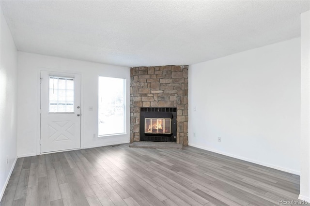 unfurnished living room with a stone fireplace, light wood-type flooring, and a textured ceiling