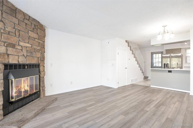 unfurnished living room with light wood-type flooring, sink, a fireplace, an inviting chandelier, and a textured ceiling