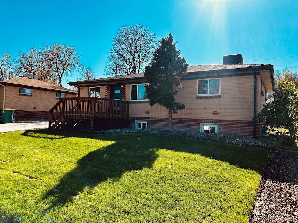 rear view of property featuring a wooden deck, a lawn, and brick siding