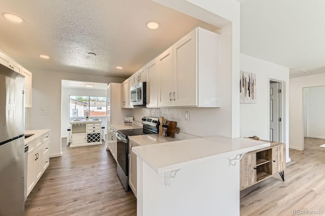 3871 Moore St, Wheat Ridge, CO 80033 - kitchen with appliances with stainless steel finishes, light wood-type flooring, recessed lighting, white cabinets, and a peninsula