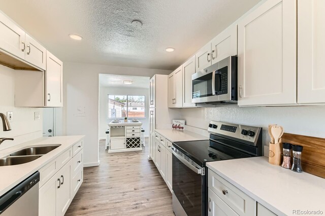 3871 Moore St, Wheat Ridge, CO 80033 - kitchen featuring appliances with stainless steel finishes, a sink, light wood-type flooring, light countertops, and white cabinetry