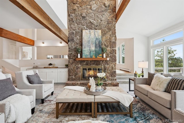 living room with baseboard heating, beam ceiling, a stone fireplace, and high vaulted ceiling