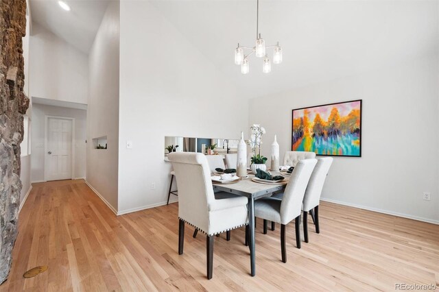 dining space featuring a notable chandelier, light hardwood / wood-style flooring, and high vaulted ceiling