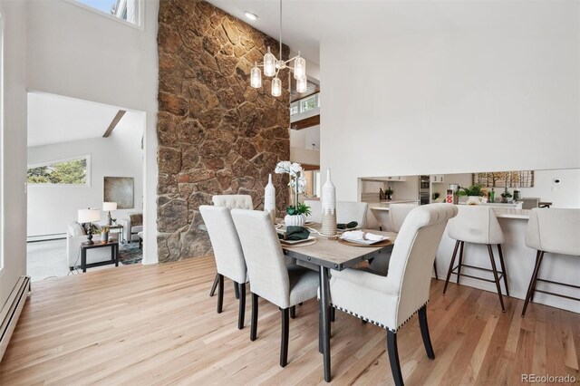 dining space with high vaulted ceiling, a chandelier, light wood-type flooring, and a baseboard heating unit