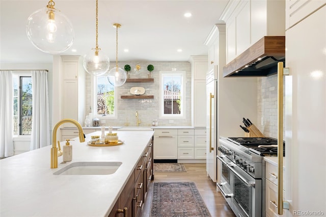 kitchen featuring a sink, wall chimney range hood, high end appliances, and light countertops