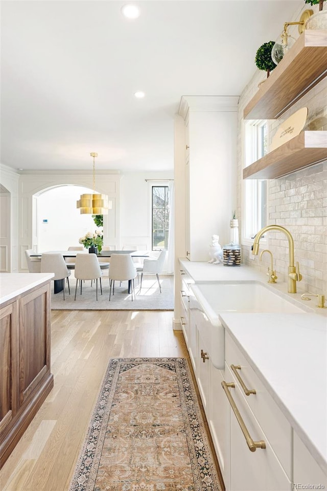 kitchen with hanging light fixtures, a sink, backsplash, light countertops, and light wood-type flooring