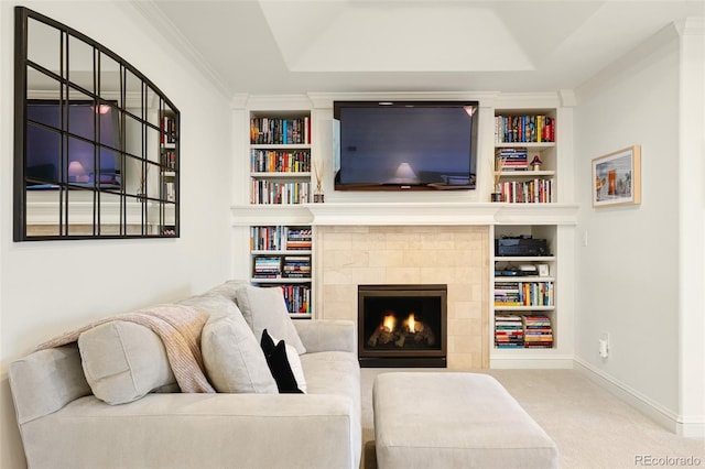 living area featuring a tile fireplace, crown molding, built in shelves, and baseboards