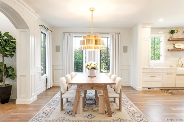 5455 E Cedar Ave, Denver, CO 80246 - dining room featuring a decorative wall, light wood-type flooring, arched walkways, wainscoting, and a chandelier