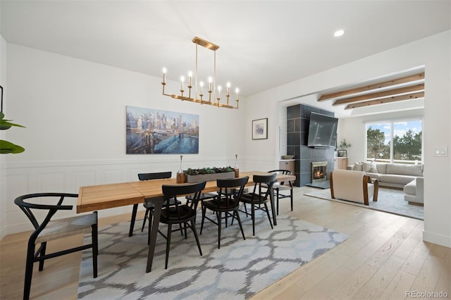 dining room featuring beam ceiling, a tiled fireplace, light hardwood / wood-style floors, and a notable chandelier