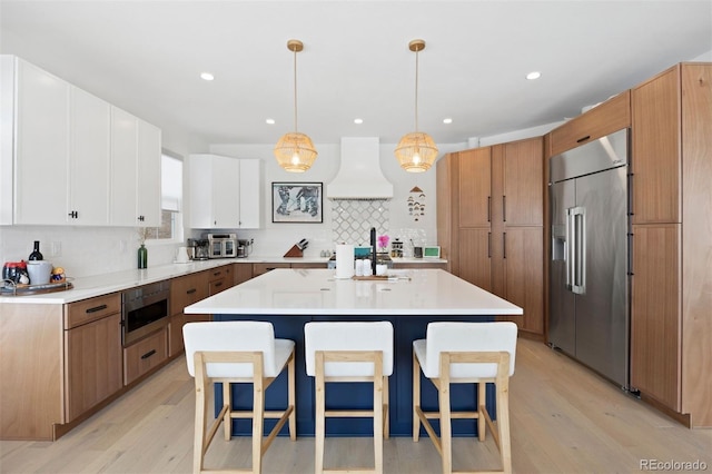 7079 S Locust Pl, Centennial, CO 80112 - kitchen with built in appliances, a kitchen breakfast bar, light wood-style flooring, and custom range hood