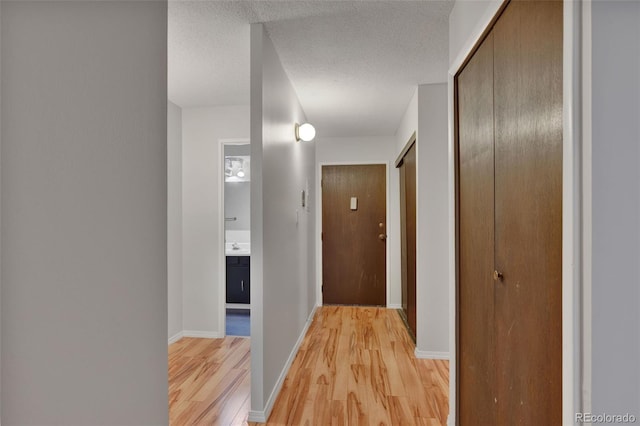 hallway with light wood-style flooring, a textured ceiling, and baseboards