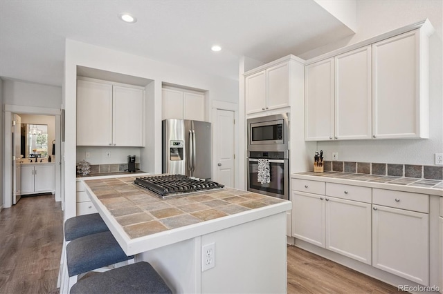 10955 Dearborne Dr, Parker, CO 80134 - kitchen featuring appliances with stainless steel finishes, tile countertops, a center island, a breakfast bar area, and light wood-type flooring