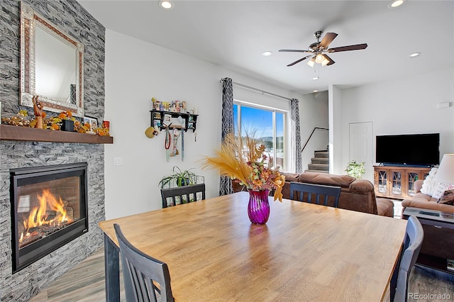 dining area featuring a stone fireplace, light wood-type flooring, and ceiling fan