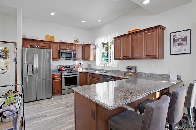 kitchen featuring kitchen peninsula, stone counters, sink, light wood-type flooring, and appliances with stainless steel finishes