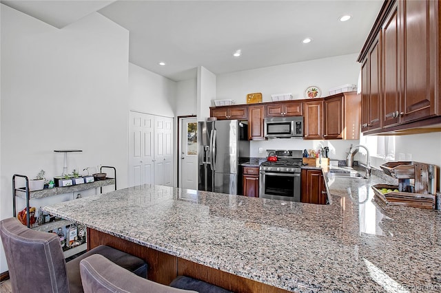 kitchen with appliances with stainless steel finishes, light stone countertops, sink, a breakfast bar area, and kitchen peninsula