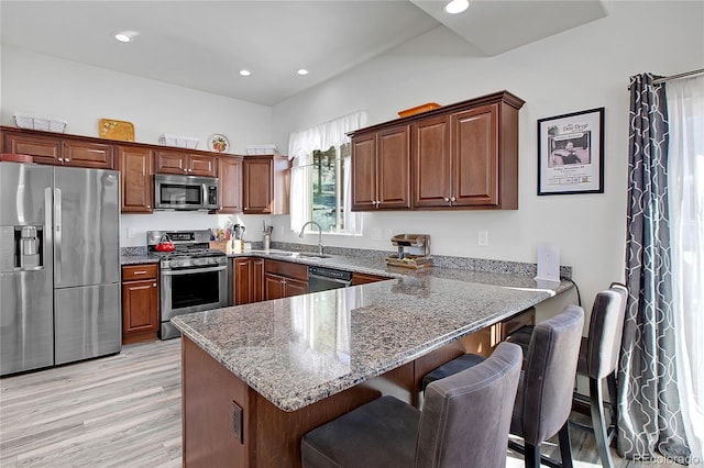 kitchen with stainless steel appliances, light hardwood / wood-style floors, kitchen peninsula, sink, and stone counters