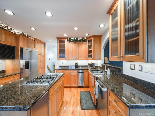 kitchen with sink, dark stone countertops, appliances with stainless steel finishes, a kitchen island, and light hardwood / wood-style floors