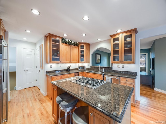 kitchen featuring sink, appliances with stainless steel finishes, dark stone countertops, a center island, and light wood-type flooring