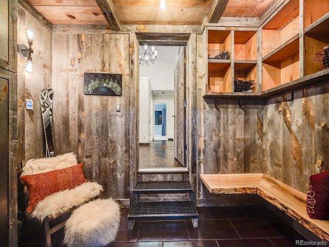 mudroom with an inviting chandelier, tile patterned floors, wooden walls, and beamed ceiling