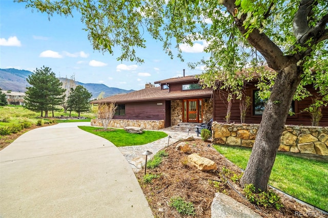 view of front of house featuring a porch, stone siding, a mountain view, and a front yard