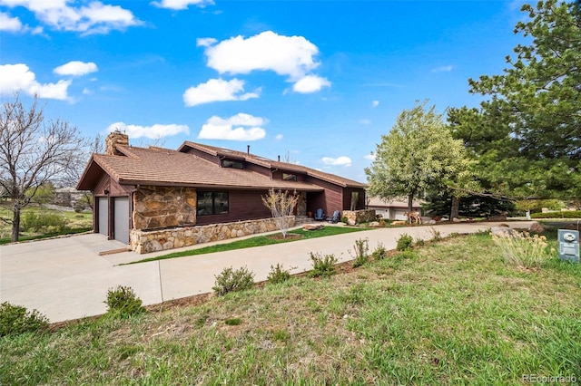 view of home's exterior with stone siding, concrete driveway, a chimney, and a garage