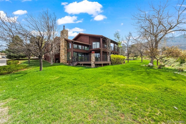 back of property featuring a chimney, a deck, and a lawn