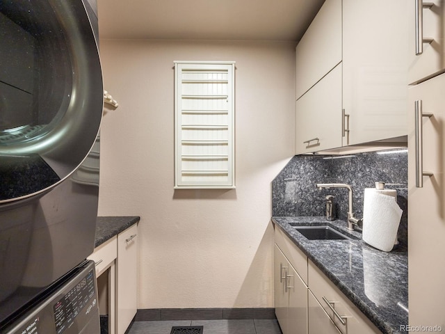 laundry area featuring baseboards, a sink, stacked washing maching and dryer, dark tile patterned flooring, and cabinet space