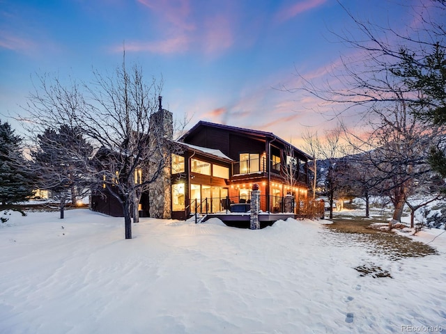 snow covered property with a chimney, a balcony, and a deck