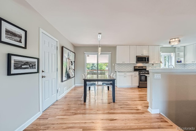 kitchen featuring white cabinetry, hanging light fixtures, light hardwood / wood-style flooring, backsplash, and appliances with stainless steel finishes