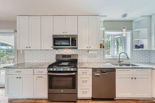 kitchen with pendant lighting, sink, light stone counters, white cabinetry, and stainless steel appliances