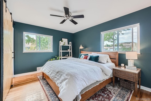 bedroom featuring hardwood / wood-style floors, ceiling fan, a barn door, and multiple windows